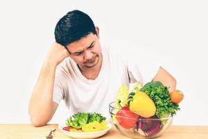 Vintage photo of Asian man showing dislike expression of fresh colorful vegetables isolated over white background