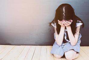 Sad Asian girl sitting on white wood floor photo