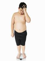 Soft focus of fat boy disappoint his fatness while standing on on weighing machine over white background photo