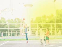 foto borrosa de niños asiáticos jugando baloncesto con luz solar cálida desde la esquina superior derecha