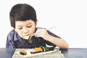 Chico encantador asiático está comiendo sushi sobre fondo blanco. foto