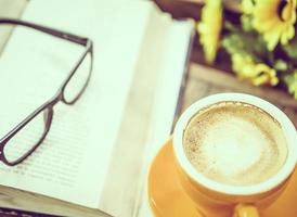 Vintage photo of a cup of coffee with book and reading glasses on wooden table, selective focused