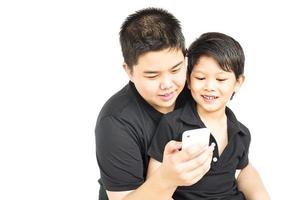 Los niños asiáticos de 14 y 7 años miran felizmente el teléfono móvil juntos aislados en blanco foto