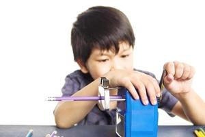 A boy is sharpening his pencil using mechanical sharpener over white background photo