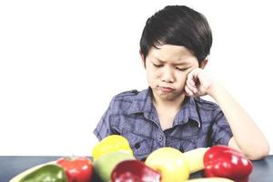 Asian boy is showing dislike vegetable expression over white background photo