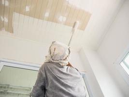 Partial focus photo of a man is painting ceiling using roller brush