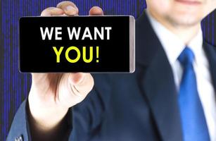 We want you word on mobile phone screen in blurred young businessman hand and digital technology background photo