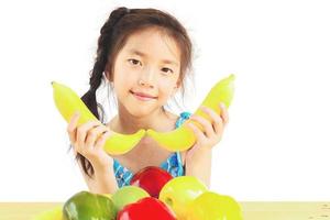 Gril asiático saludable mostrando expresión feliz con variedad de frutas y verduras de colores sobre fondo blanco. foto