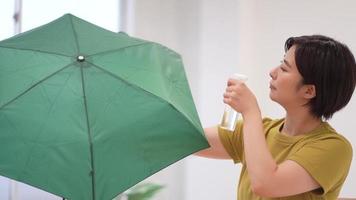 una mujer rociando un spray repelente al agua en un paraguas plegable