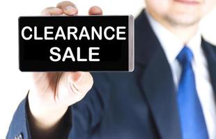 CLEARANCE SALE word on mobile phone screen in blurred young businessman hand over white background, business concept photo