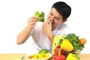 hombre asiático que muestra disgusto por la expresión de verduras frescas y coloridas aisladas sobre fondo blanco foto