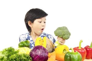 niño sano asiático que muestra una expresión feliz con una variedad de verduras frescas y coloridas sobre fondo blanco foto