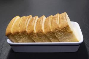 Homemade sliced butter cake in white ceramic tray over black background - famous homemade cake dessert concept photo