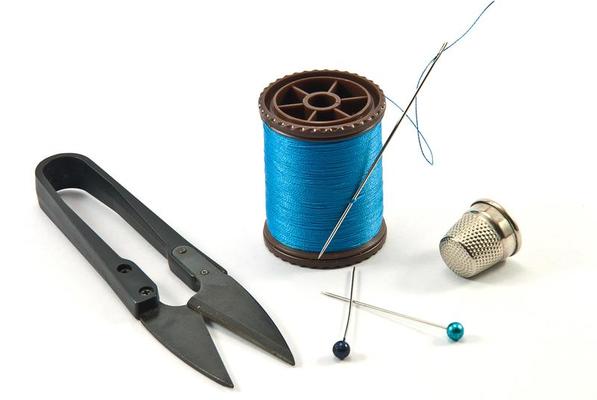 Needle with thread, thimble, bobbin with black thread and scissors