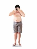 Soft focus of fat boy disappoint his fatness while standing on on weighing machine over white background photo