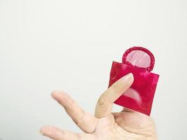 la mano de una dama que muestra un condón rojo y un paquete con fondo de espacio en blanco foto