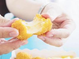 Hand is holding a stretch cheese ball ready to be eaten over blue table background photo