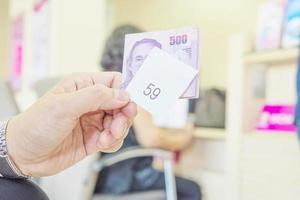 Man is holding queue card with 500 Baht Thai bank note while waiting in the modern bank reception area photo