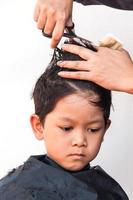 un peluquero le corta el pelo a un niño sobre fondo blanco, concéntrese en sus ojos derechos foto