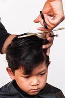 un peluquero le corta el pelo a un niño sobre fondo blanco, concéntrese en sus ojos foto