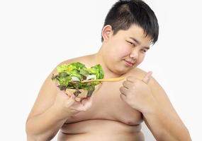 un niño gordo está felizmente comiendo ensalada de verduras foto