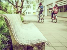 Vintage style photo of bench sitting with blurred bicycling student in the campus