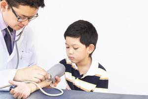 niño asiático siendo examinado por un médico varón usando estetoscopio y monitor de presión arterial sobre fondo blanco foto