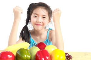 Chica sana asiática mostrando expresión feliz con variedad de frutas y verduras de colores sobre fondo blanco. foto