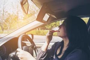 Woman making up her face using lipstick while driving car, unsafe behavior photo