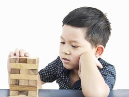 un niño asiático está jugando un juego de torre de bloques de madera para practicar habilidades físicas y mentales. la foto está aislada en blanco.