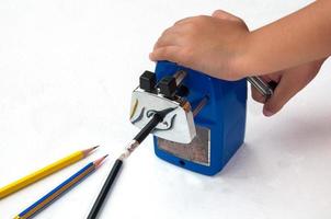 A boy is sharpening his pencil using mechanical sharpener over white background photo