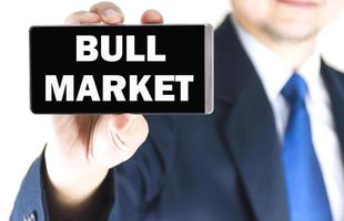 BULL MARKET word on mobile phone screen in blurred young businessman hand over white background, business concept photo