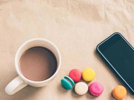 Vintage photo of coffee cup with macaroon and mobile phone over brown paper background