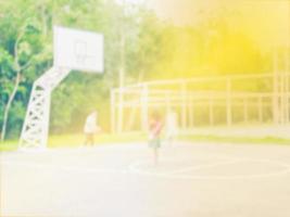 foto borrosa de niños asiáticos jugando baloncesto con luz solar cálida desde la esquina superior derecha