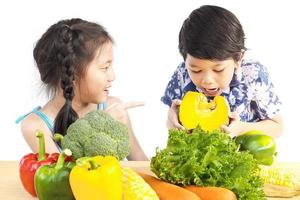 Asian boy and girl showing enjoy expression with fresh colorful vegetables isolated over white background photo