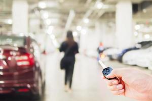 la mano está usando el mando a distancia del coche sobre una foto borrosa de una mujer que camina peligrosamente en una zona de aparcamiento