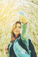 joven asiática tomando una foto selfie usando un teléfono móvil con fondo de árbol pumaria