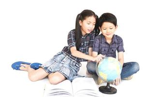 Los niños y niñas asiáticos de 7 y 10 años están estudiando el mapa del mundo, aislados sobre fondo blanco foto