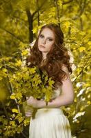 Young woman holding a bunch of yellow maple leaves. Autumn portrait of young woman. Red haired girl in autumn forest photo