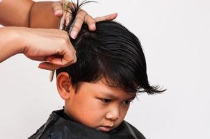 un peluquero le corta el pelo a un niño sobre fondo blanco, concéntrese en sus ojos derechos foto