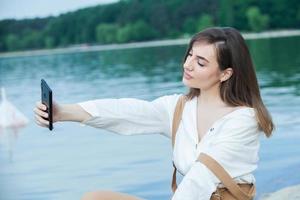 chica al aire libre enviando mensajes de texto en su teléfono móvil. chica con teléfono. retrato de un mensaje de texto de mujer feliz en su teléfono. foto