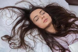 Girl sleeps in a white bed at home. Young woman sleeping in sleepwear on the white linen in bed at home, top view. photo