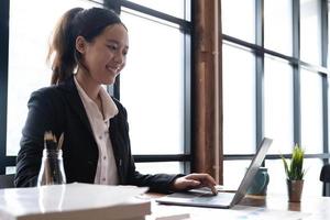 Beautiful young asian woman sitting at coffee shop using laptop. Happy young businesswoman sitting at table in cafe with tab top computer. photo