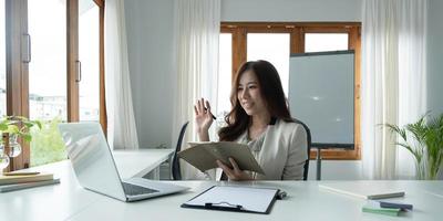 Asian female talking about sale report in video conference. Asian team using laptop and tablet online meeting in video call.Working from home remotely. photo