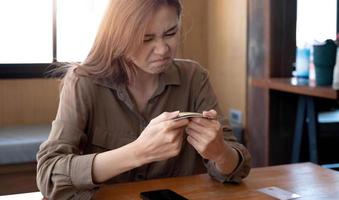 Angry and furious millennial asian woman breaking a credit card or debit card with her hands, having a financial problems. photo