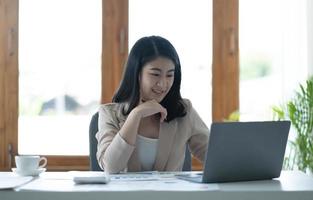 Beautiful young asian woman sitting at coffee shop using laptop. Happy young businesswoman sitting at table in cafe with tab top computer. photo