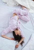 Girl sleeps in a white bed at home. Young woman sleeping in sleepwear on the white linen in bed at home, top view. photo