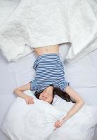 chica duerme en una cama blanca en casa. mujer joven durmiendo en ropa de dormir en el lino blanco en la cama en casa, vista superior. foto