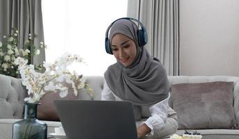 tutoría en línea. joven profesora musulmana haciendo videollamadas con estudiantes, hablando con la cámara de una laptop, sentada en el sofá en casa foto