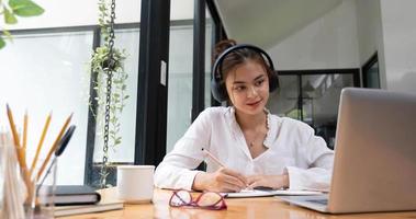 una chica sonriente con auriculares sentada en el escritorio mira el estudio de la pantalla de un portátil en línea, una joven feliz e inteligente con auriculares toma un curso web o entrena en una computadora, concepto de educación distante